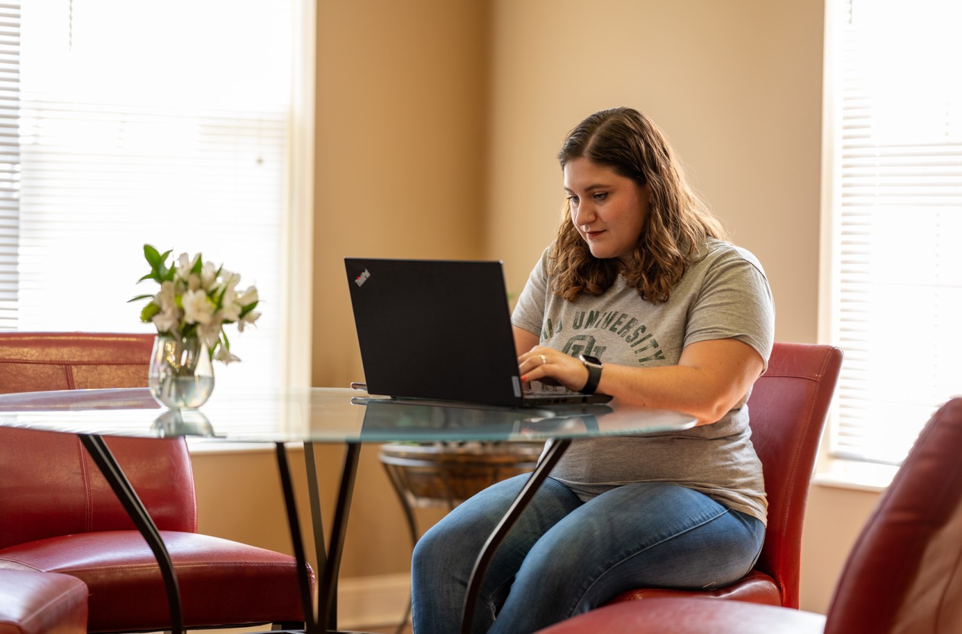 A woman in an OU t-shirt sitting down using a laptop.