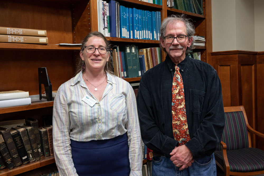 Two people in semi-formal attire standing next to eachother behind some books, smiling.