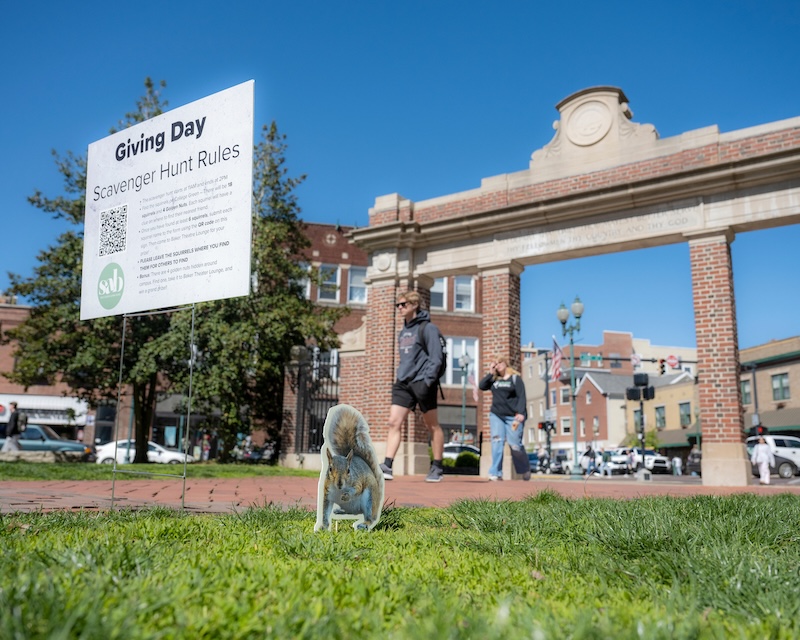 OHIO students walk by a squirrel image in the grass on the College Green near the Alumni Gateway