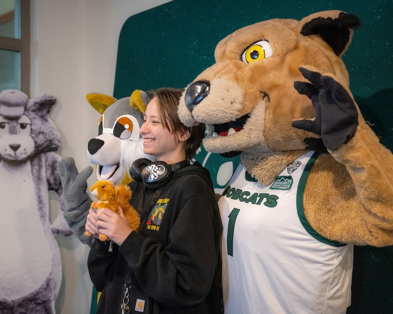 An OHIO student holds a stuffed animal squirrel while standing between a squirrel mascot and the Rufus mascot and posing for a photo.