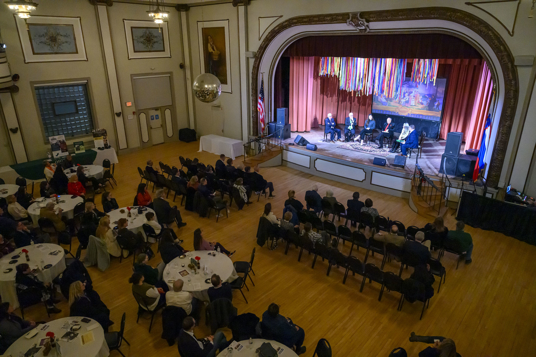 An overhead image of a large crowd watching and listening to a presentation on stage at the Slovenian Museum and Archives event in Cleveland