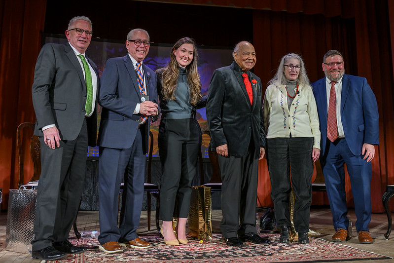 The speakers at the event stand together on the stage.