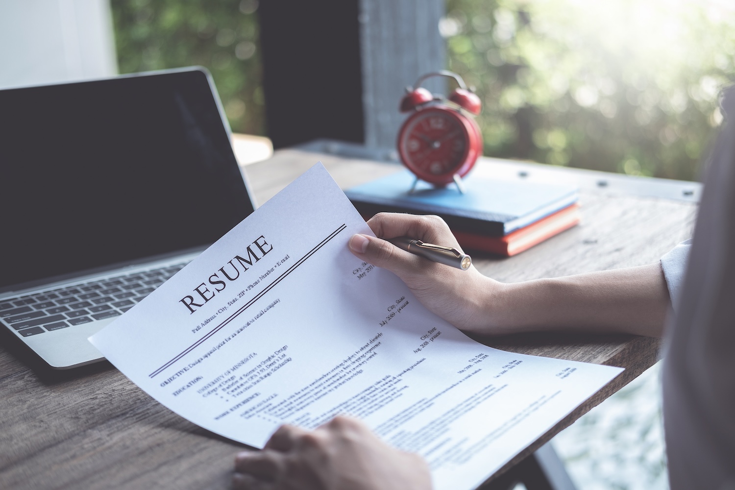 First-person perspective of someone holding their resume with their laptop in the background. 