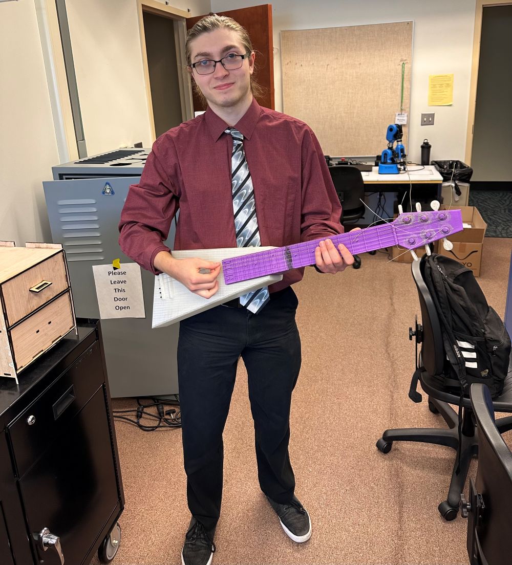 Petrie standing with his 3D printed guitar. 