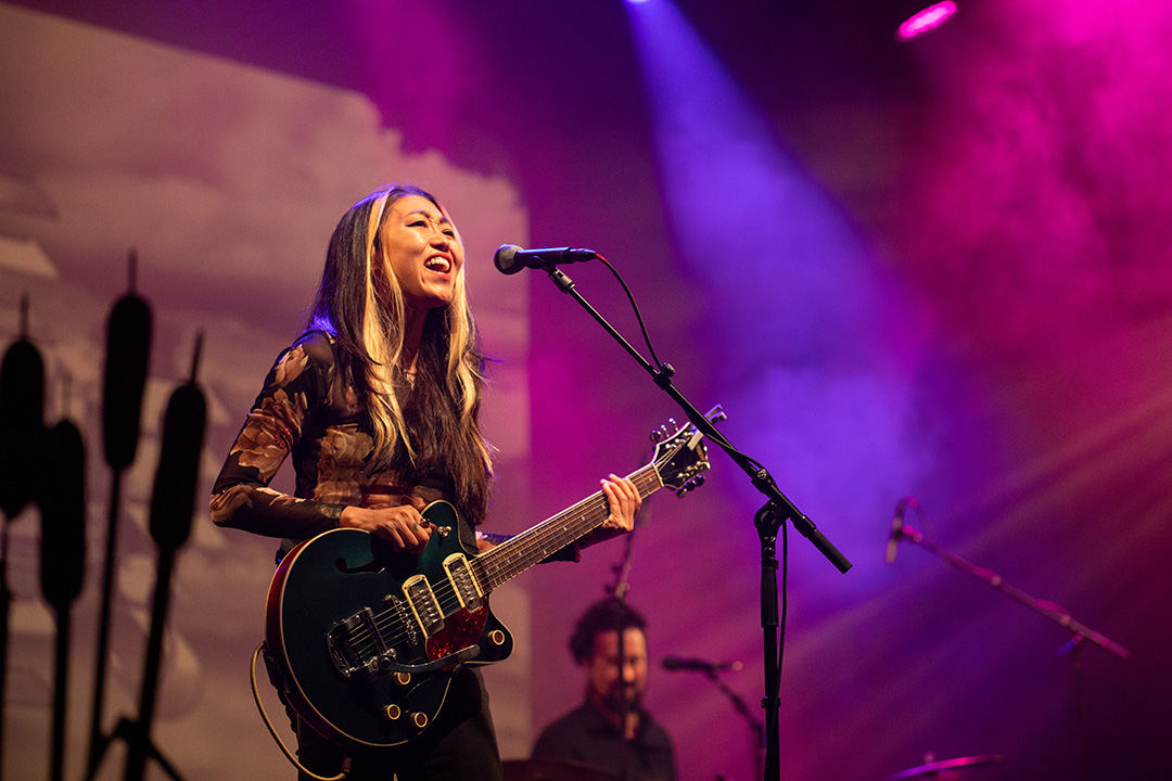 Lee Emi of The Crane Wives sings and plays guitar on the stage of Memorial Auditorium.