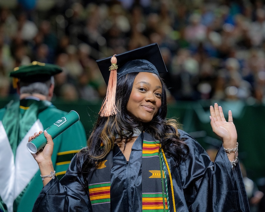 a student wearing a cap and gown poses happily holding her new diploma