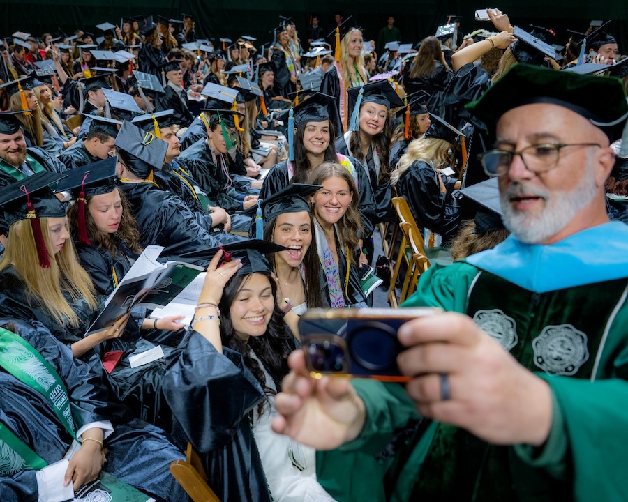 a faculty member takes a selfie with graduating students at the 2026 Spring Commencement ceremony