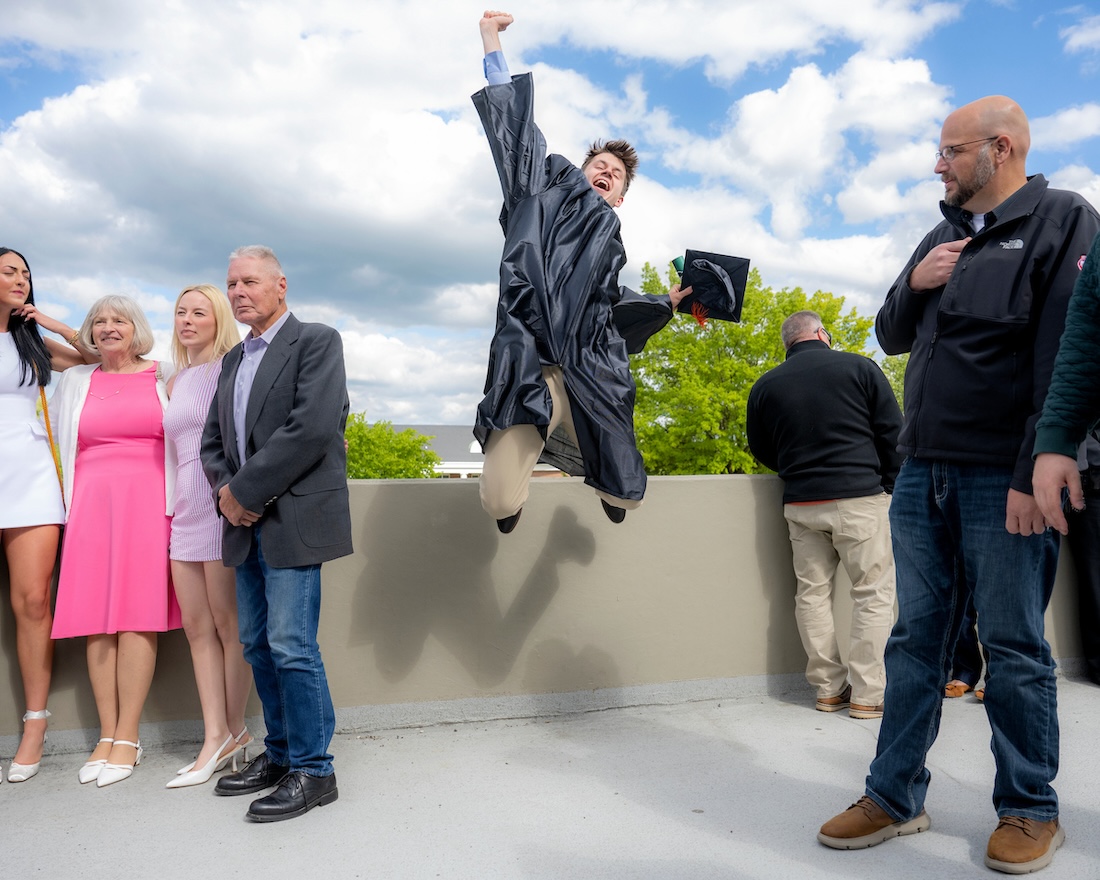 a new graduate in a cap and gown leaps in the air with a triumphant fist raised