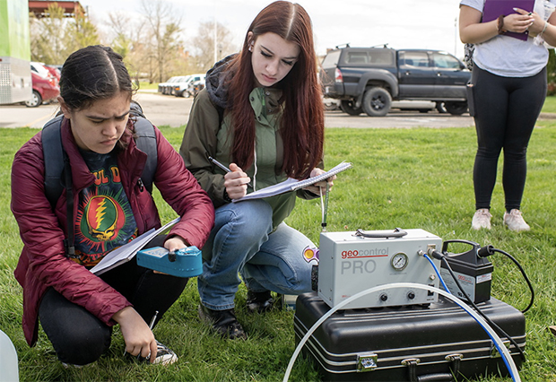 Two geology students study paperwork during a lab at Ohio University beside geology equipment set up on the ground.