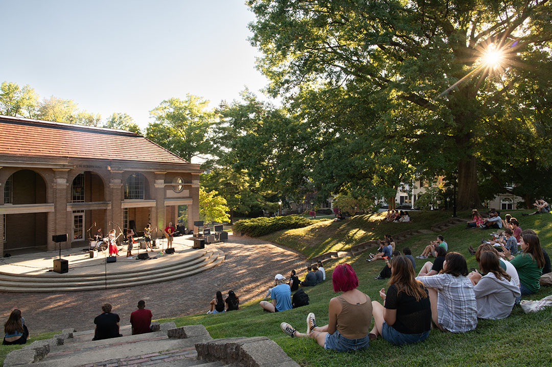 Students sit on the hillside amphitheater behind Scripps Hall to watch a musical performance.