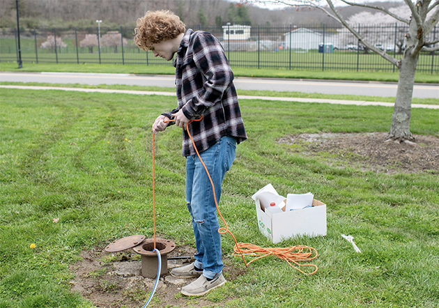 Geology student pulling a tool attached to a line from a hole in the ground during fieldwork.