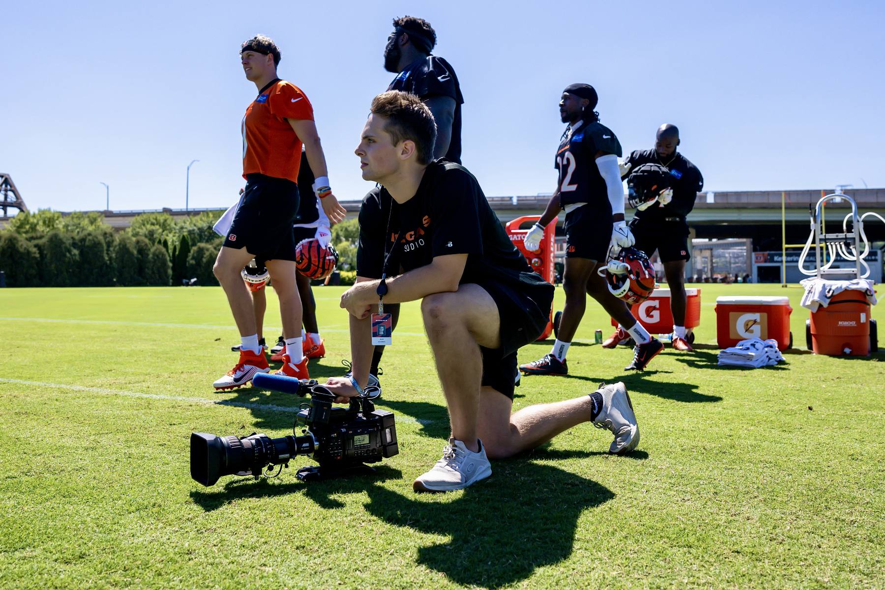 Jack Cowman kneels beside Cincinnati Bengals quarterback Joe Burrow on the field, camera in hand