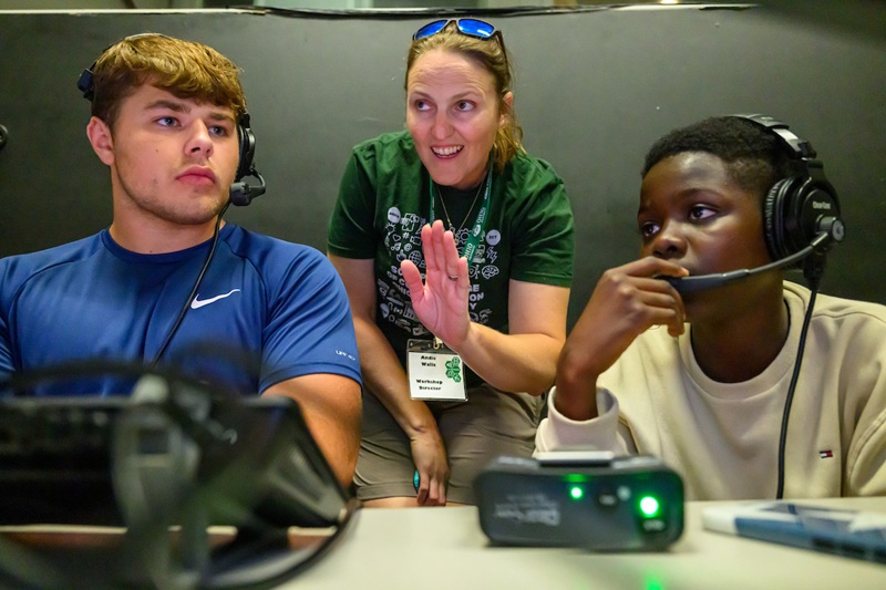 Andie Walla talks to two students who are wearing headsets and working on a video project at the camp.