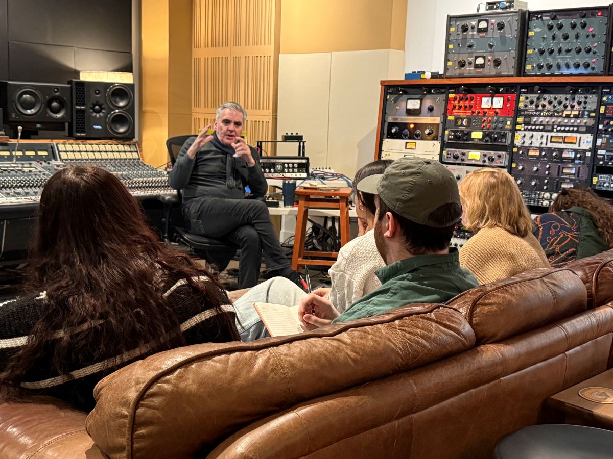 Producer Jim Eno sits before a group of students, hands in the air as he coaches them in the studio.