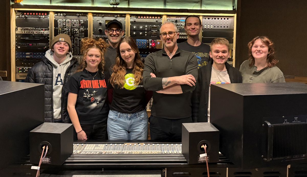 Producer Joel Hamilton stands and smiles in his studio with a group of six students and Josh Antonuccio.