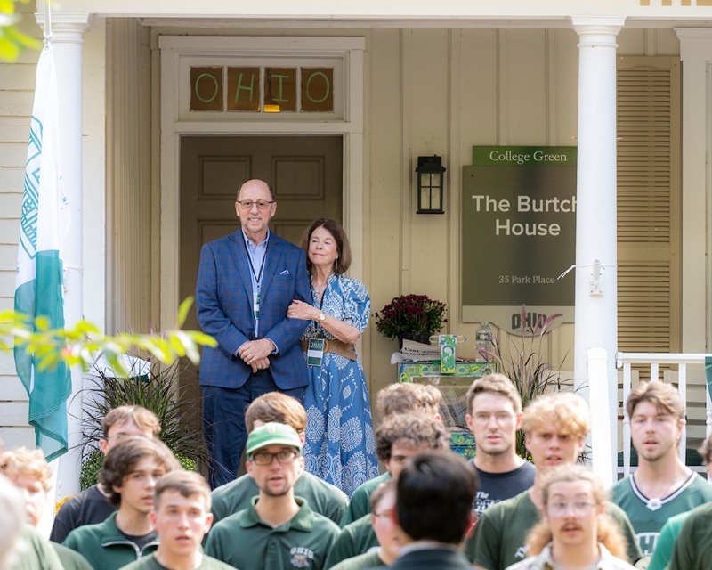 Bruce and Janie Burtch stand on the porch of The Burtch House while OHIO students sing in front of the porch during the dedication ceremony.