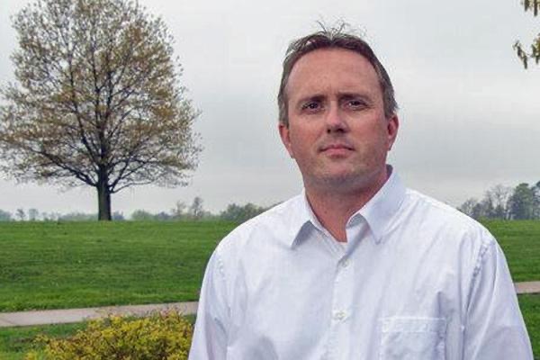 Dr. Kevin Spiker poses in front of landscape for a headshot. 