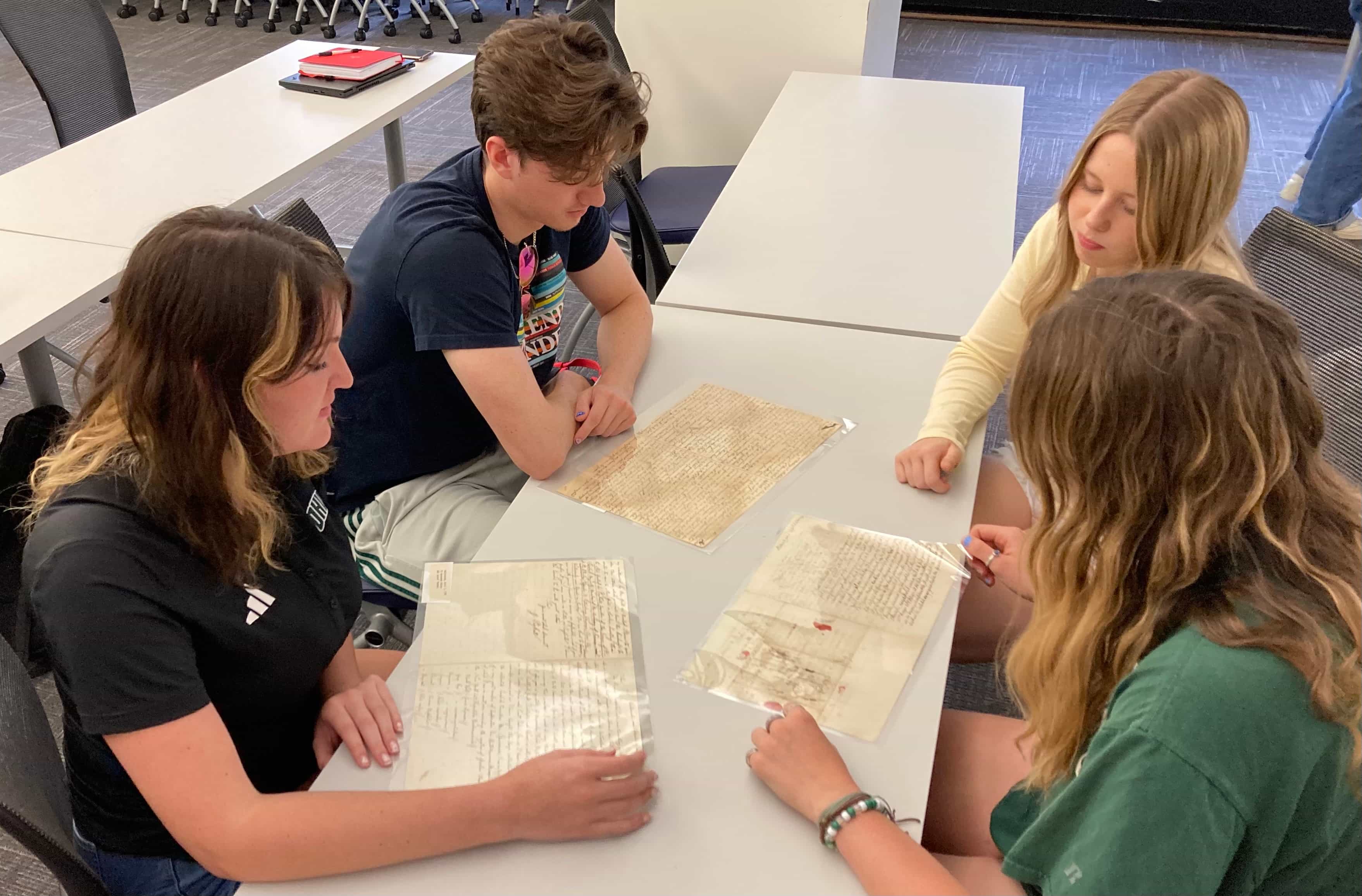 Four students sit at a table looking at historical documents