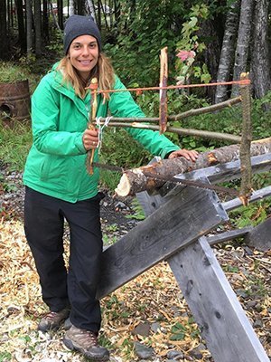 Regina Beach is pictured this past fall during a nine-week Bushcraft School course in northern Maine where she lived off the grid and learned survival skills such as shelter-building and tool construction, including making the frame for this bucksaw.