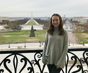 Nicole Dascenzo, who participated in the Scripps Semester in D.C. program during the 2017-18 academic year, is pictured on a balcony in Washington, D.C., with the Washington Monument in the background.