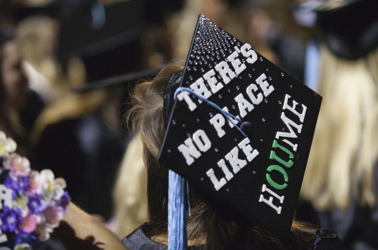 Student wearing cap at commencement that reads There's No Place Like HOUME