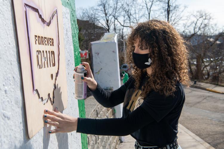 Person placing a stencil with words Forever OHIO and shape of state of Ohio against concrete wall