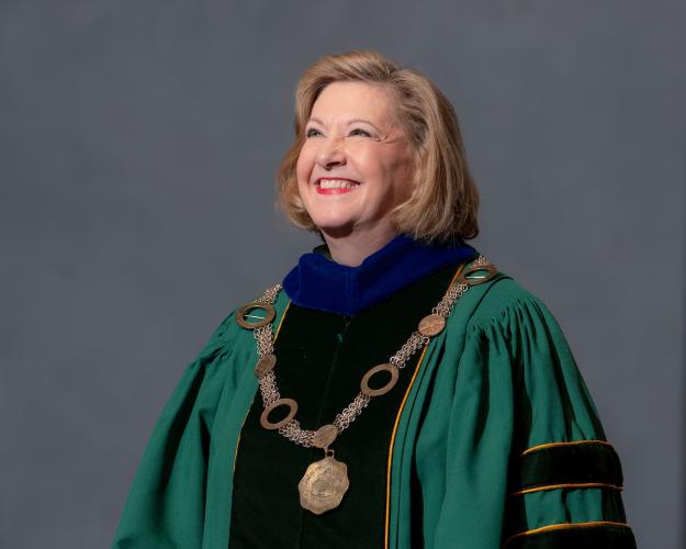 President Lori Stewart Gonzalez stands on stage wearing academic regalia and the presidential seal