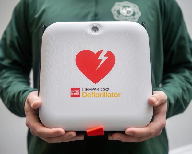 An emergency defibrillator is held by a person wearing a green Ohio University shirt
