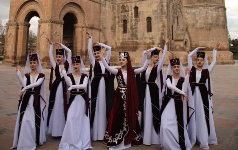 Group of young women in traditional Armenian garb in front of large historic building