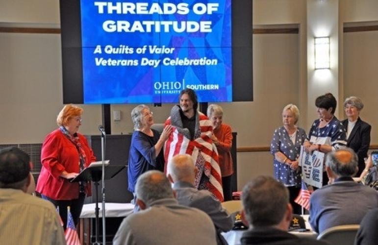 Veteran stands smiling, wrapped in quilt