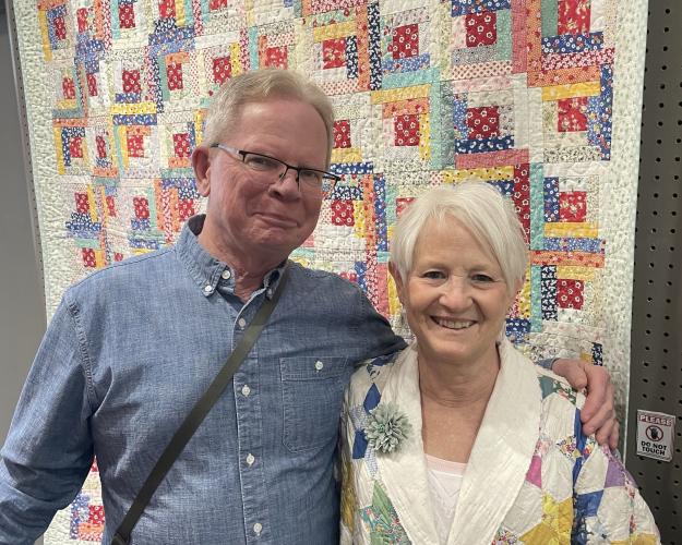 Man and Wife, standing in front of handmaid quilt