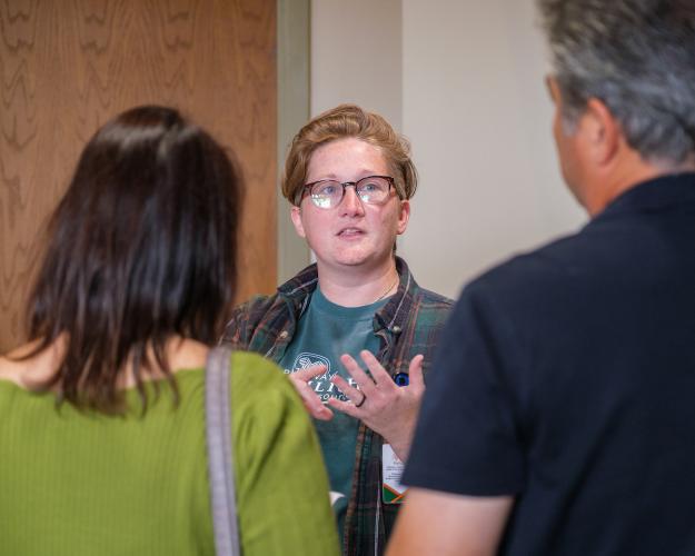 Woman speaks with two people, gesturing with her hands
