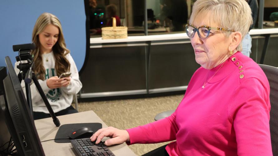 woman sitting behind a computer, with OHIO student in the background