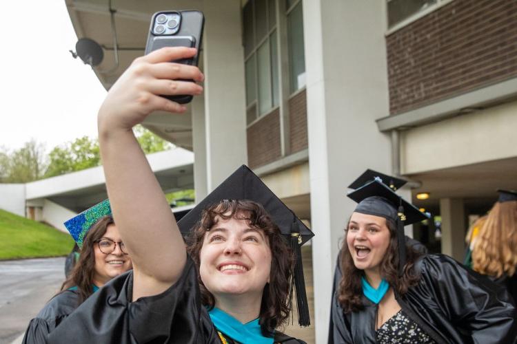 Nikki Wood and other OHIO graduates take a selfie while wearing Commencement caps and robes and standing next to the Convocation Center.