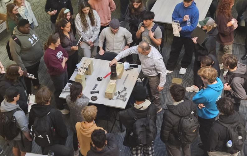 A Learning Community instructor works on a project at a table while a large crowd of students watches