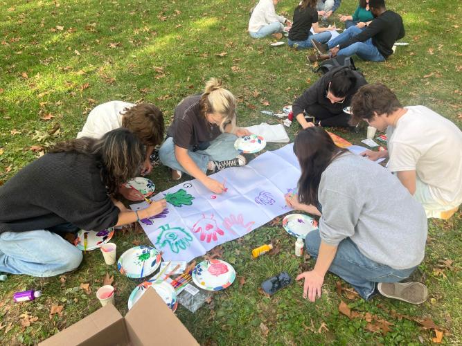 OHIO students paint together on canvases outside in the grass