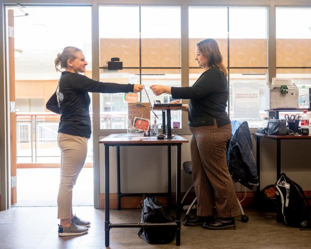 An OHIO student hands a card to a Cats Cupboard employee while at a desk at the food pantry