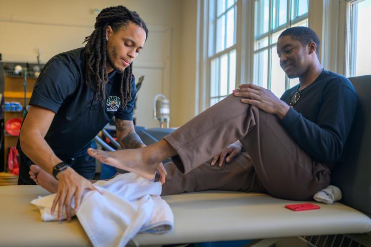 patient sitting on table with athletic trainer working on his leg
