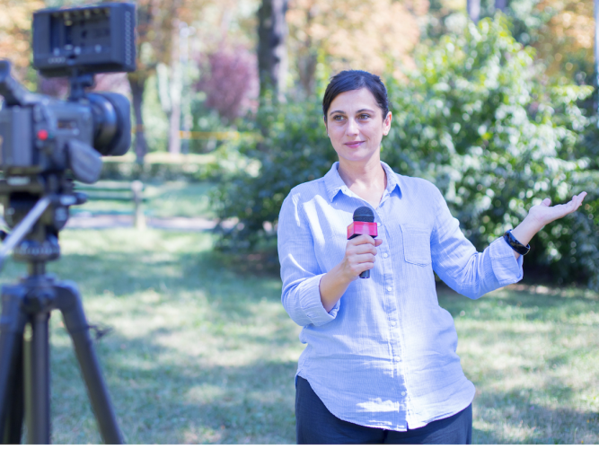 student reporter standing outside holding a microphone and facing the camera