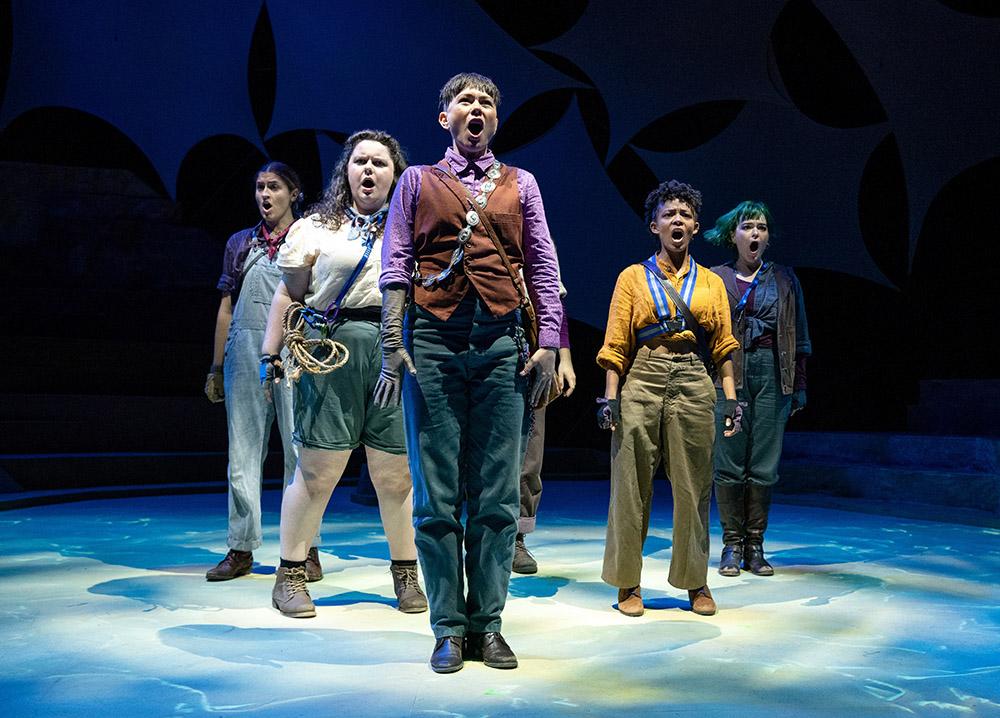 Actors stand on stage in a V shape facing forward