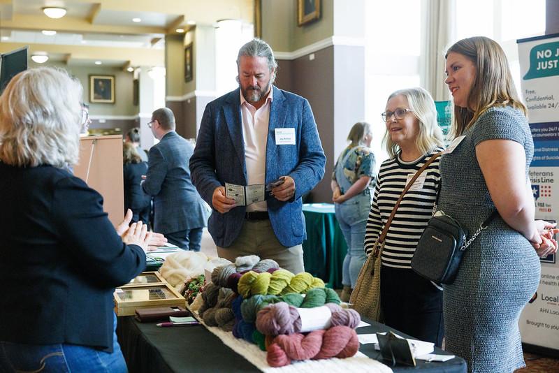 Attendees at the State of the Region Conference talk to a person at a booth that has bundles of yarn on the table in the Baker University Center