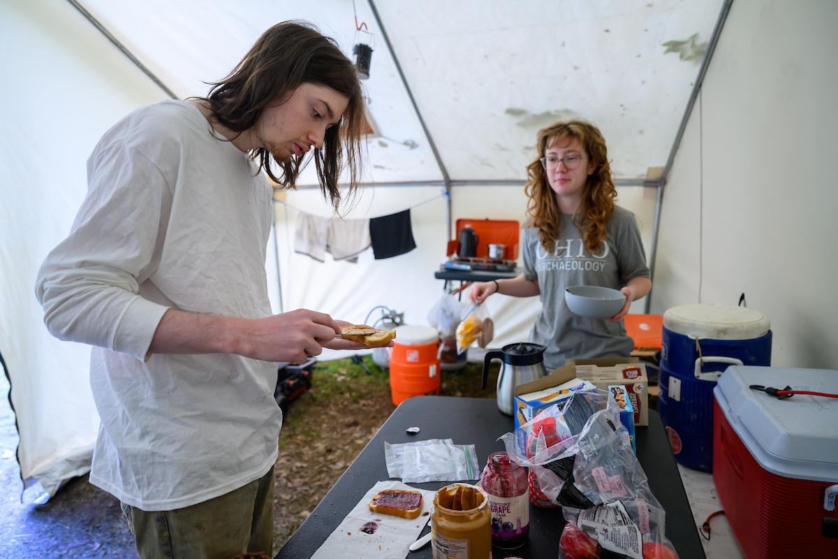 Students stand in an archeological field tent with artifacts