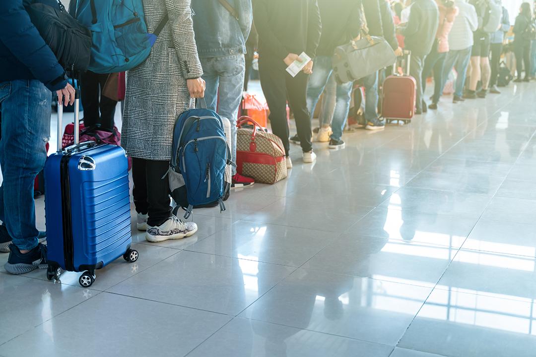 Airport travelers stand in a line with their luggage.