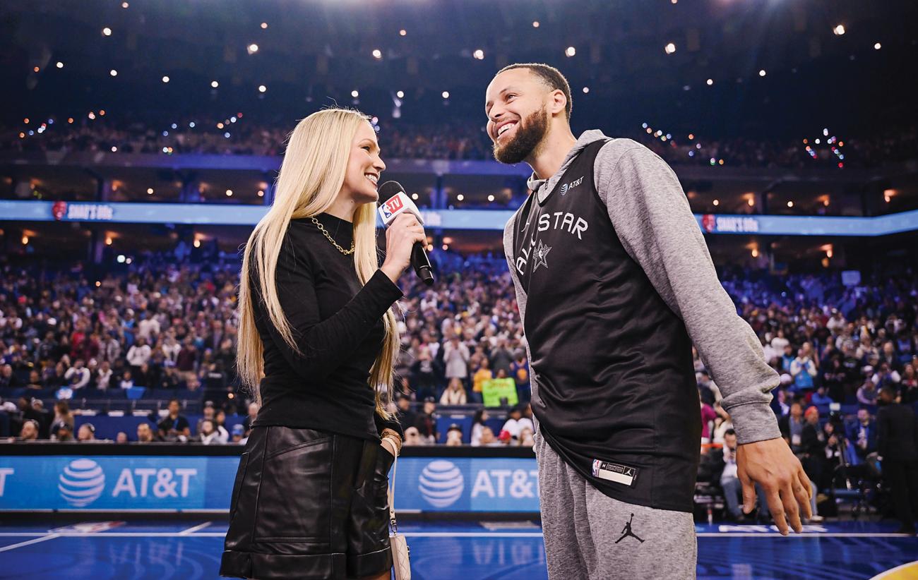 sports reporter Allie LaForce holds a mic and speaks to basketball player Stephen Curry in a packed basketball arena