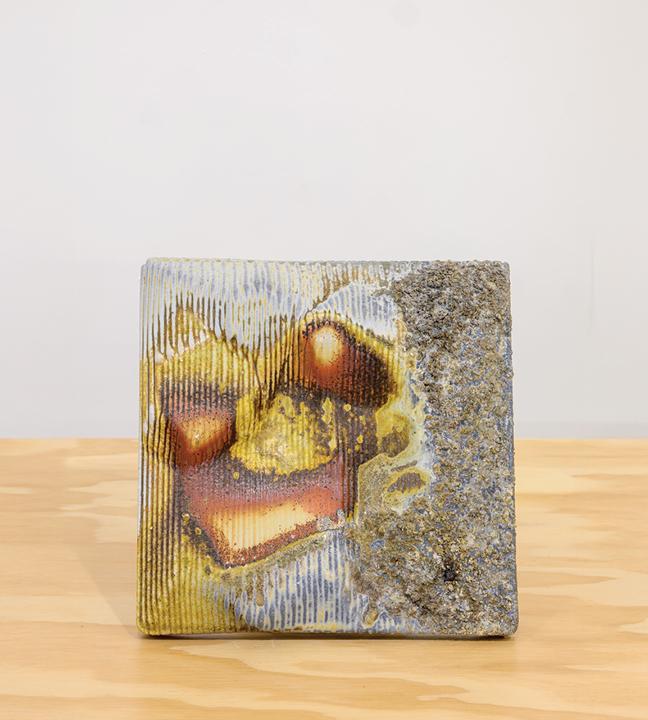 a square ceramic piece with abstract detailing in shades of gray, brown, yellow, orange, and light blue