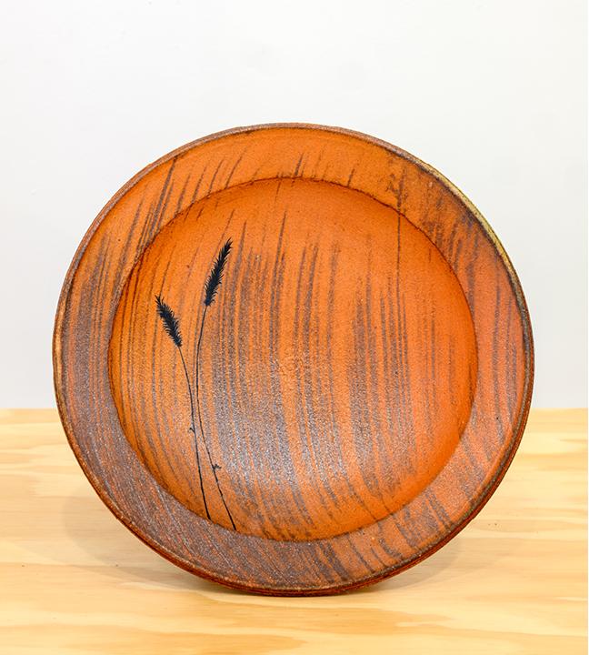 a shallow orange ceramic bowl with black and gray painted images of grass and wheat