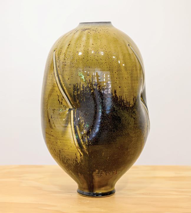 a mustard yellow ceramic vase that’s wide at the center and narrower at top and bottom, with indents in the middle and abstract black details