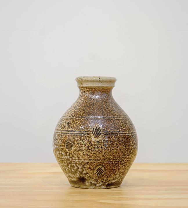 a small speckled dark and light brown ceramic bottle that’s widest at the middle and narrower on top and bottom