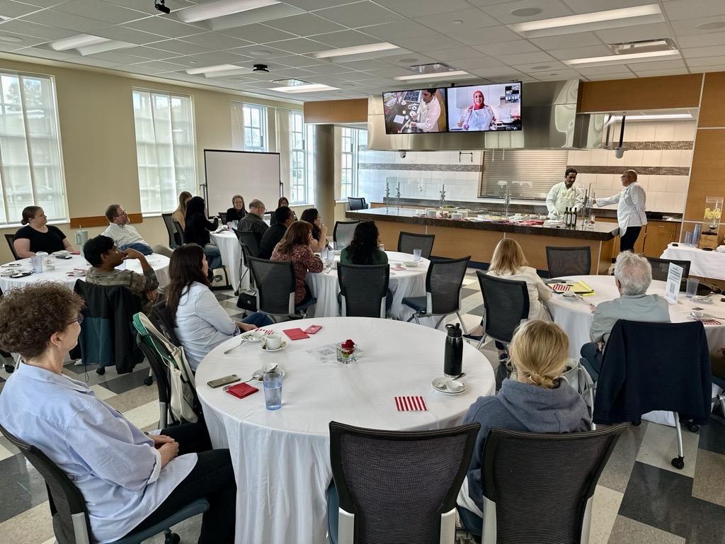 Yvonne Maffei  presents the cooking demonstration on the video screen before a large crowd seated at tables