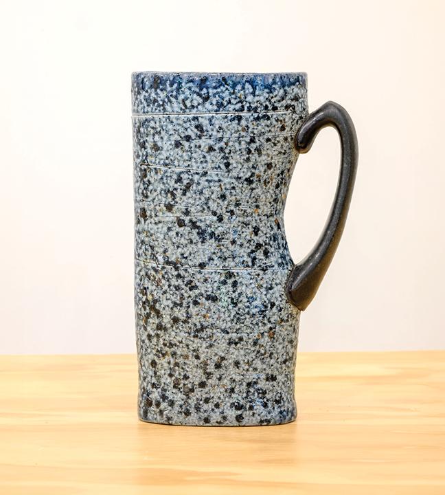 a tall speckled blue and black ceramic cup with a handle